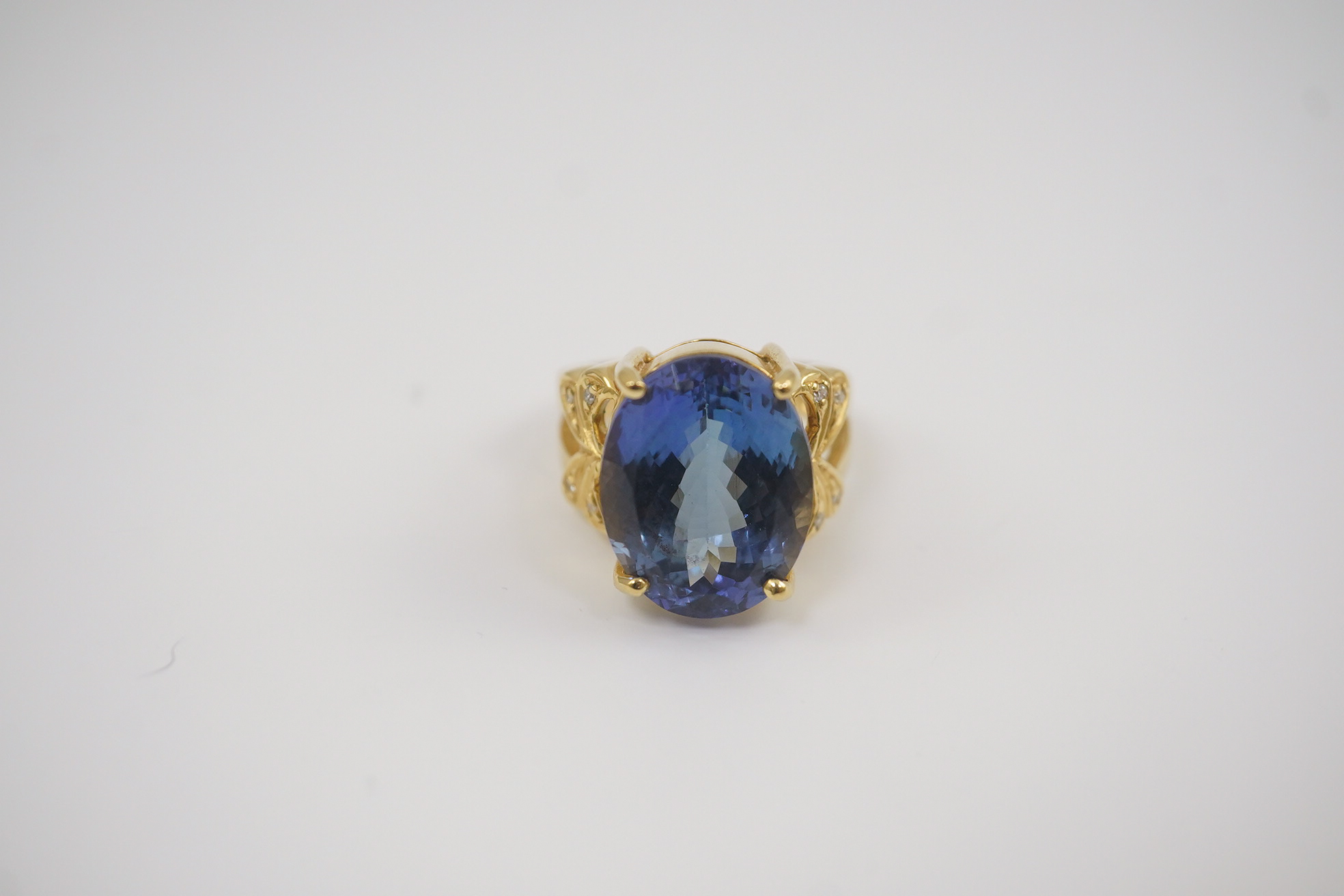 A modern 18ct gold and single stone oval cut tanzanite set dress ring, with eight stone diamond chip set shoulders